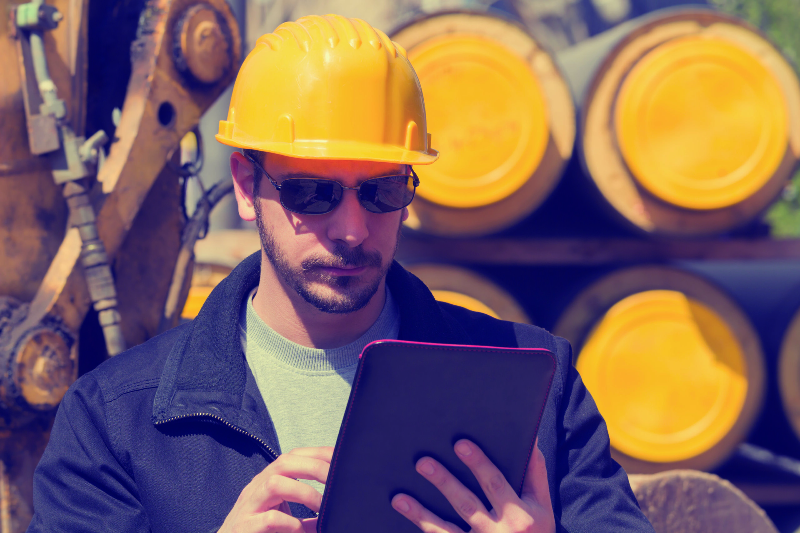man in yellow hard hard wearing safety glasses looking at a tablet